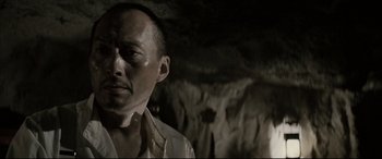 Movie still from “Letters from Iwo Jima” (2006), directed by Clint Eastwood – A man in a white shirt is standing in a cave; Close Up shot, Low angle