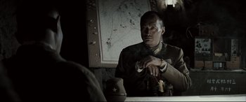 Movie still from “Letters from Iwo Jima” (2006), directed by Clint Eastwood – A man sitting in front of a map looking at his watch; Close Up shot, Over the shoulder angle