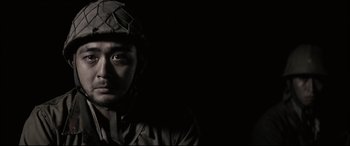 Movie still from “Letters from Iwo Jima” (2006), directed by Clint Eastwood – A man wearing a helmet is looking into the camera; Close Up shot, Low angle
