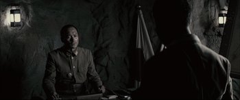 Movie still from “Letters from Iwo Jima” (2006), directed by Clint Eastwood – A man sitting at a table in front of a flag; Medium shot, Over the shoulder angle