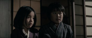 Movie still from “Letters from Iwo Jima” (2006), directed by Clint Eastwood – Two young asian children in traditional garb looking into the camera; Close Up shot, Low angle