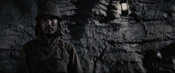 Movie still from “Letters from Iwo Jima” (2006), directed by Clint Eastwood – A man wearing a hat and a jacket standing in front of a stone wall; Close Up shot, High angle