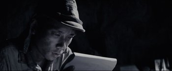 Movie still from “Letters from Iwo Jima” (2006), directed by Clint Eastwood – A man wearing a hat looking down at a tablet computer; Close Up shot, Low angle