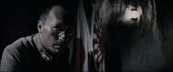 Movie still from “Letters from Iwo Jima” (2006), directed by Clint Eastwood – A man with glasses standing in front of flags; Close Up shot, Low angle