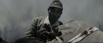 Movie still from “Letters from Iwo Jima” (2006), directed by Clint Eastwood – A man wearing a hat is looking at something in his hand; Close Up shot, Over the shoulder angle