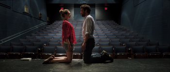 A man kneeling down next to a woman in front of an audience
