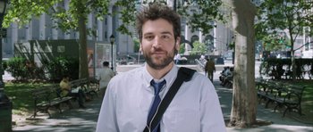A man with a beard and a blue tie is listening to music