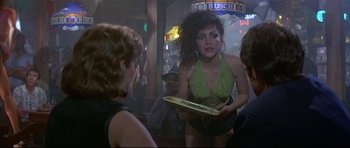 Movie still from “Licence to Kill” (1989), directed by John Glen – A woman in a green top holding a tray in front of two other women; Medium shot, Over the shoulder angle