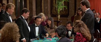 Movie still from “Licence to Kill” (1989), directed by John Glen – A group of people sitting around a table playing cards; Medium shot, High angle