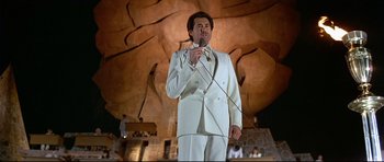 Movie still from “Licence to Kill” (1989), directed by John Glen – A man wearing a white suit and holding a microphone; Wide shot, Low angle