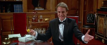 Movie still from “Licence to Kill” (1989), directed by John Glen – A man in a tuxedo sitting at a dinner table; Medium shot, Low angle