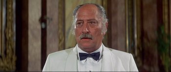 Movie still from “Licence to Kill” (1989), directed by John Glen – An older man in a white suit and a bow tie; Close Up shot, Low angle