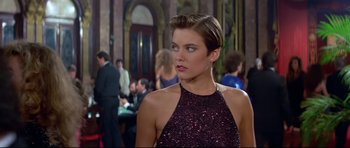 Movie still from “Licence to Kill” (1989), directed by John Glen – A beautiful woman in a red dress standing next to a table; Medium shot, Over the shoulder angle