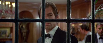 Movie still from “Licence to Kill” (1989), directed by John Glen – A man in a suit and bow tie looking through a window; Close Up shot, Over the shoulder angle