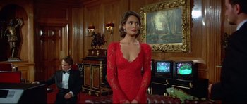 Movie still from “Licence to Kill” (1989), directed by John Glen – A woman in a red dress standing in front of a tv; Medium shot, Over the shoulder angle