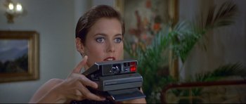 Movie still from “Licence to Kill” (1989), directed by John Glen – A woman holding a camera in her hands; Close Up shot, Over the shoulder angle