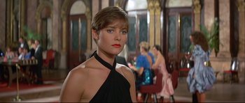 Movie still from “Licence to Kill” (1989), directed by John Glen – A woman in a black dress standing in front of other women; Close Up shot, Over the shoulder angle