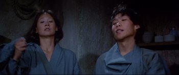 Movie still from “Licence to Kill” (1989), directed by John Glen – A man and a woman standing next to each other in front of a stone wall; Close Up shot, Low angle