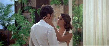 Movie still from “Licence to Kill” (1989), directed by John Glen – A man and a woman standing next to each other in front of bushes; Close Up shot, Over the shoulder angle