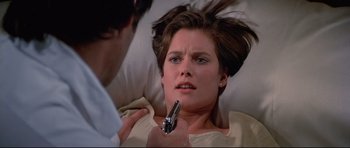 Movie still from “Licence to Kill” (1989), directed by John Glen – A woman laying in a hospital bed with a man holding a cell phone; Close Up shot, Over the shoulder angle