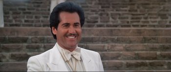 Movie still from “Licence to Kill” (1989), directed by John Glen – A man in a white suit smiling for the camera; Close Up shot, Low angle