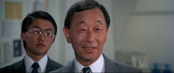 Movie still from “Licence to Kill” (1989), directed by John Glen – An older asian man in a suit and tie; Close Up shot, Low angle