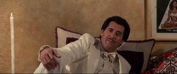 Movie still from “Licence to Kill” (1989), directed by John Glen – A man in a white suit sitting on a couch; Medium shot, Low angle
