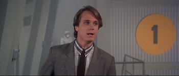 Movie still from “Licence to Kill” (1989), directed by John Glen – A man in a suit and tie standing in a room; Close Up shot, Over the shoulder angle