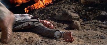 Movie still from “Licence to Kill” (1989), directed by John Glen – A man laying on the ground in front of a fire pit; Medium shot, Overhead angle