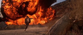 Movie still from “Licence to Kill” (1989), directed by John Glen – A man running in the desert near a huge fire; Wide shot, Low angle