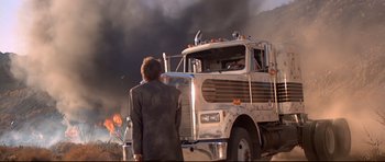 Movie still from “Licence to Kill” (1989), directed by John Glen – A man standing in front of a large truck; Wide shot, Low angle