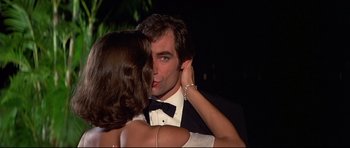 Movie still from “Licence to Kill” (1989), directed by John Glen – A man and a woman kissing in front of a dark background; Close Up shot, Low angle