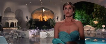 Movie still from “Licence to Kill” (1989), directed by John Glen – A woman in a blue dress in front of a mirror in a room; Medium shot, Low angle