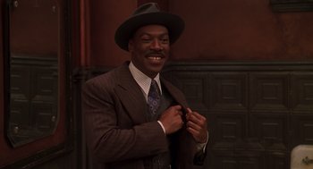 Movie still from “Life” (1999), directed by Ted Demme – A man in a suit and a hat is smiling; Medium shot, Low angle