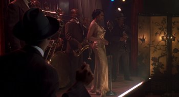Movie still from “Life” (1999), directed by Ted Demme – A group of people on a stage with a woman in a gold dress; Wide shot, Over the shoulder angle