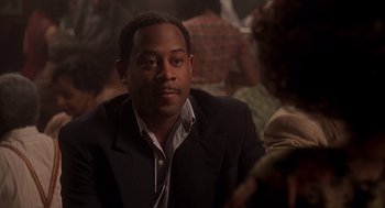 Movie still from “Life” (1999), directed by Ted Demme – A man in a suit sitting in front of other people; Close Up shot, Over the shoulder angle