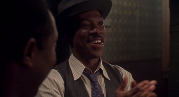 Movie still from “Life” (1999), directed by Ted Demme – A man wearing a hat and a tie talking to someone; Close Up shot, Over the shoulder angle
