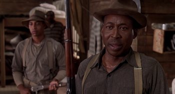 Movie still from “Life” (1999), directed by Ted Demme – A man in a hat holding a rifle in front of another man; Close Up shot, Low angle