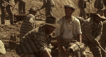Movie still from “Life” (1999), directed by Ted Demme – A group of men sitting next to each other on a dirt field; Medium shot, High angle