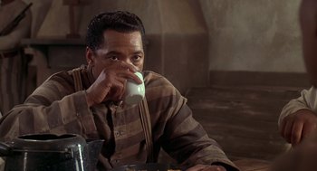 Movie still from “Life” (1999), directed by Ted Demme – A man sitting at a table drinking from a cup; Medium shot, Over the shoulder angle