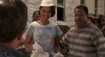 Movie still from “Life” (1999), directed by Ted Demme – A woman in a dress and a white hat smiling for the camera; Medium shot, Over the shoulder angle