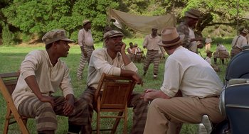Movie still from “Life” (1999), directed by Ted Demme – A group of men sitting in the grass talking to each other; Wide shot, High angle