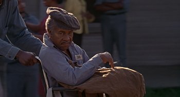 Movie still from “Life” (1999), directed by Ted Demme – An older man sitting in a chair with a cigarette in his hand; Medium shot, High angle