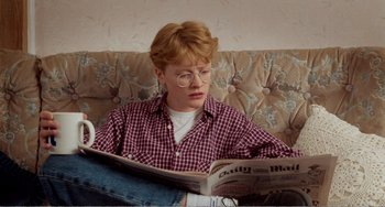 Movie still from “Life Is Sweet” (1990), directed by Mike Leigh – A person sitting on a couch reading a newspaper; Medium shot, High angle