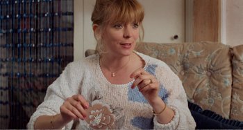 Movie still from “Life Is Sweet” (1990), directed by Mike Leigh – A woman sitting on a couch holding a cell phone; Close Up shot, Over the shoulder angle