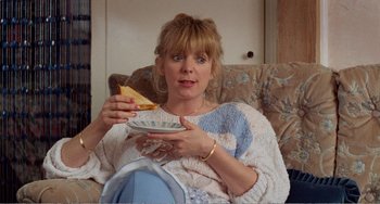 Movie still from “Life Is Sweet” (1990), directed by Mike Leigh – A woman sitting on a couch holding a plate of food; Medium shot, High angle