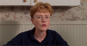 Movie still from “Life Is Sweet” (1990), directed by Mike Leigh – A person with glasses is sitting in a kitchen; Close Up shot, Low angle