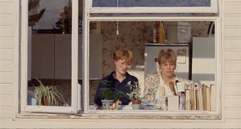 Movie still from “Life Is Sweet” (1990), directed by Mike Leigh – Two women sitting at a table in front of a window; Medium shot, Over the shoulder angle