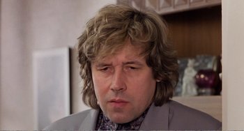 Movie still from “Life Is Sweet” (1990), directed by Mike Leigh – A person wearing a suit and tie; Close Up shot, Low angle