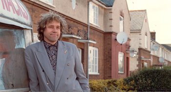 Movie still from “Life Is Sweet” (1990), directed by Mike Leigh – A man standing in front of a brick building; Medium shot, Low angle